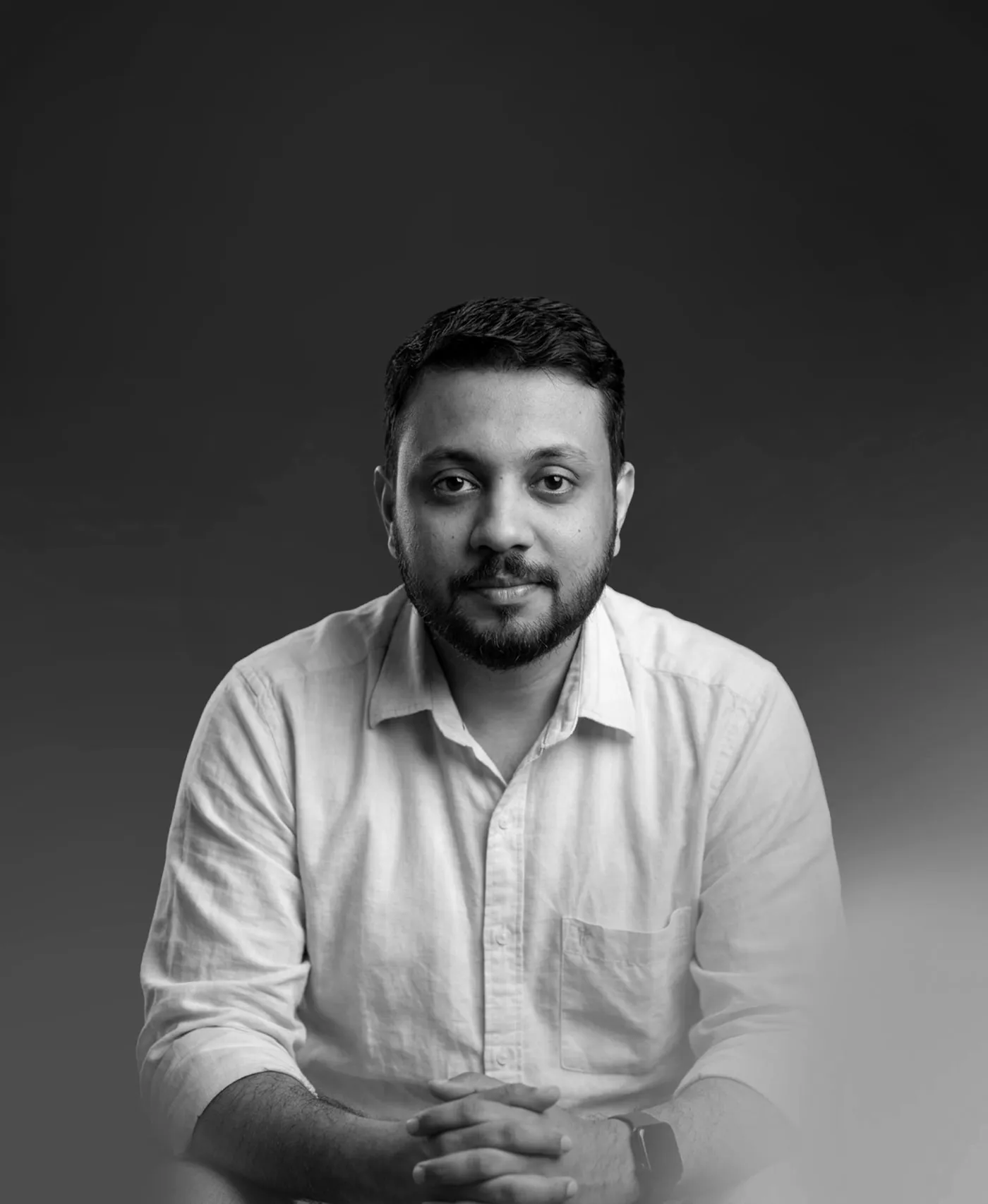 Black-and-white portrait of Abin T Jose seated, hands clasped, in a light shirt